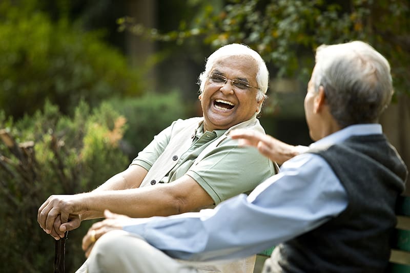 Senior aged gentlemen sitting on park bench and laughing